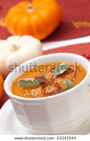 Closeup of a cup of hot delicious spicy roasted pumpkin soup with pumpkin crisps, sage and sesame seads.