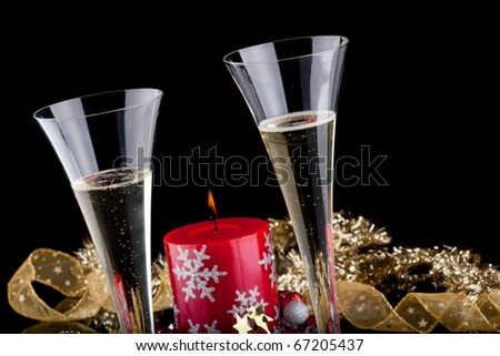 Closeup of flutes of champagne, candles and Christmas decoration on black background.