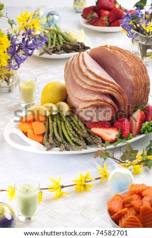 Festive glazed ham for Easter celebration dinner garnished with asparagus, carrots, strawberry, and lemon wedges.