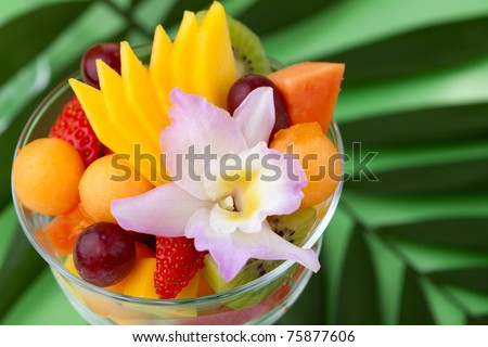 Closeup of serving of fresh tropical fruit salad in cocktail glass. Kiwi, melon, papaya, mango, red grapes, strawberry and orchid flower.