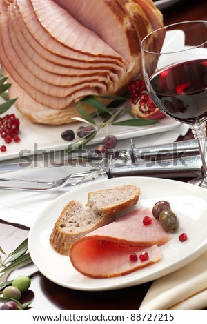 Closeup of plate with ham , bread and olives on dinning table set with glazed whole baked sliced ham, garnished with pomegranate.