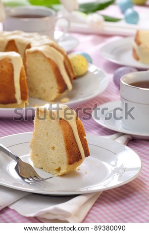 Piece of Lemon Easter cake with lemon icing, served with cup of tea, and decorated with painted eggs