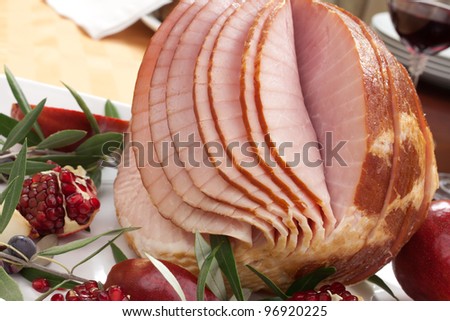 Dinning table set with glazed whole baked sliced ham, garnished with pomegranate, olives, and red pears.