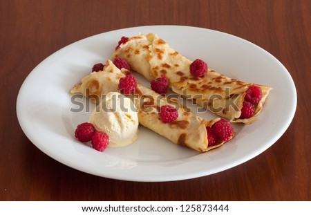 Crepes with raspberries and vanilla ice cream on a white plate