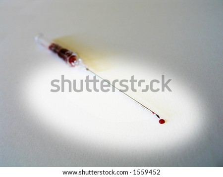 A hollow medical needle with a drop of blood after a bleed.