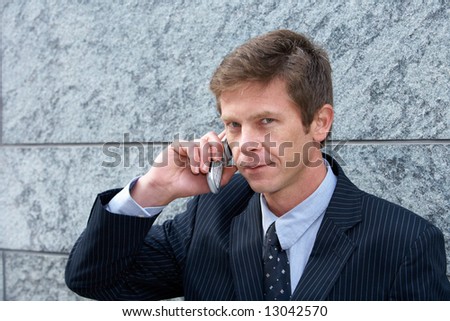 Man on cell phone by building wall, looking at camera