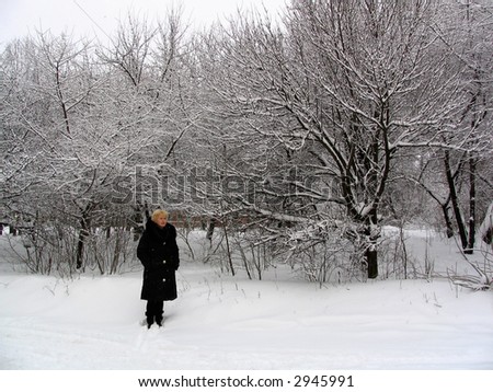 middle-aged woman stand still under light snow in winter park