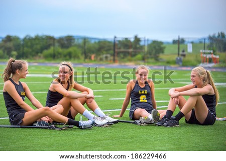 Members of girls Lacrosse team sitting on field talking after practice.