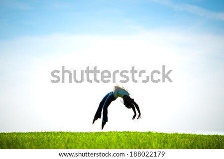African American woman captured in mid-air doing a back flip in a fresh Spring field. Silhouetted.