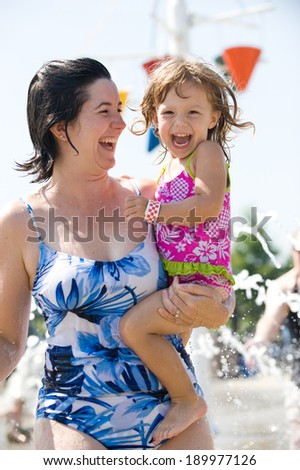 Ear to ear smiles on a mother with her 2 year old daughter at a water park. Lots of splashing water visible in both foreground and background.