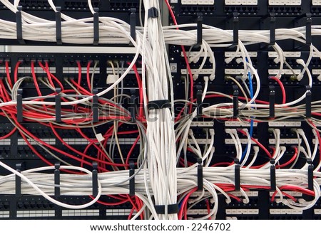 Bundles of Ethernet cables weave and wind through wire guides on a massive LAN network patch panel.