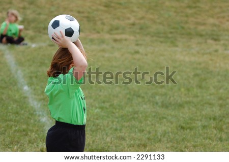 A young girl soccer player stands on the sideline about to throw the ball back into play.