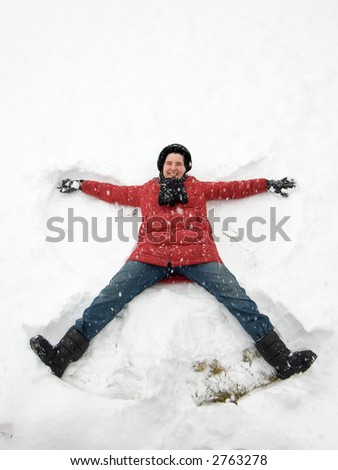 Woman in red coat lays down in the falling snow to make a snow angel.
