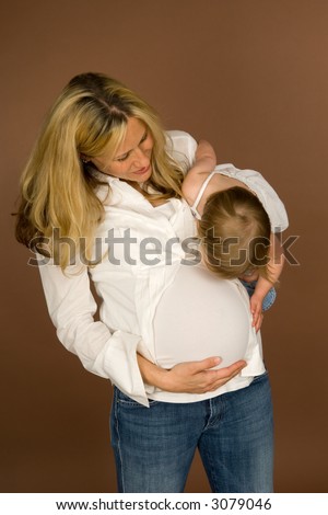 Young, pregnant mother holds her daughter who is interested in her belly. Mother is in her third trimester.