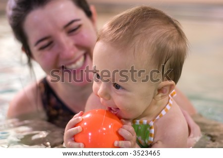 Mother and young daughter playing and having a great time during baby swimming lessons.