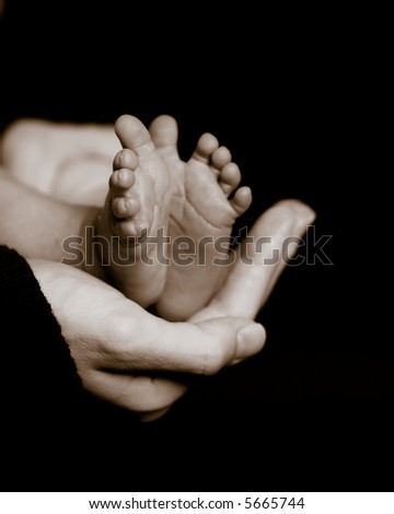 Mother holds her newborn\'s tiny feet in the palm of her hand. Sepia toned and slight grain for a classic, timeless look. Shallow DOF focus on mother\'s hand and the toes closest to the viewer.