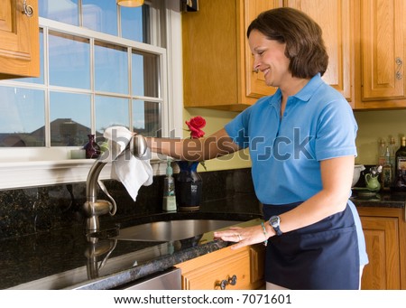 Cheerful maid polishing a brushed nickel faucet in a high end luxury kitchen. Cleaning woman has a smile with eyes focused on the task at hand.