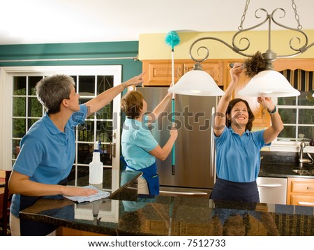 Team of three women housekeepers / maids cleaning a modern kitchen. Maid on the left is pointing, reminding the maid with the extension pole duster not to miss a spot.