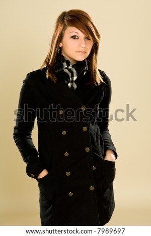 Gothic / Scene Kid style clothing worn by a red headed teen. It\'s a black pea coat with buttons and a black and white scarf. Creme background.