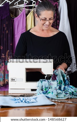 Happy senior woman dressmaking with sewing machine