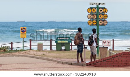 DURBAN, SOUTH AFRICA - January 31, 2015: Two Men looking out to sea in front of an Information Sign along the promenade at the beach in Umhlanga Rocks