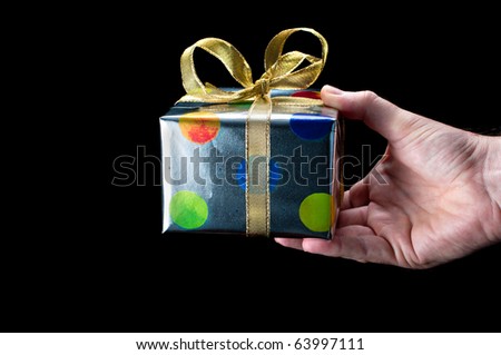 Man's hand holding a colorful silver present with a gold bow on a black background