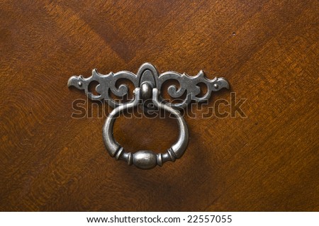 Pewter silver metal handle or knocker on dark rich mahogany wood dresser door.