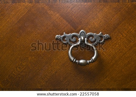 Pewter silver metal handle or knocker on dark rich mahogany wood dresser door.
