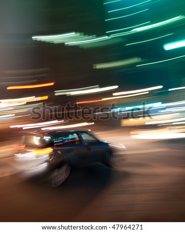 Small car in motion in downtown urban scene. Motion blur and light streaks convey busy city night concept.