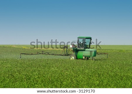 Farm tractor with sprayer attached spraying crop in field.