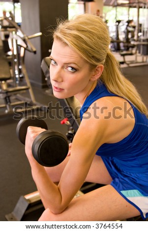 Beautiful blond woman lifting weights in a fitness center.