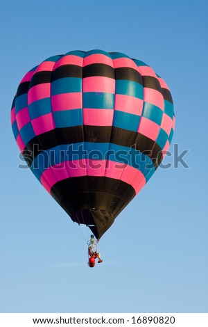 A colorful hot air balloon at a festival is suspended in mid-air on a clear day.