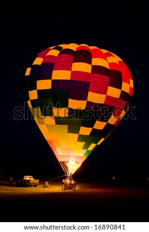 A hot air balloon team is lighting the balloon\'s propane burner while its tethered to the ground at night to produce a \