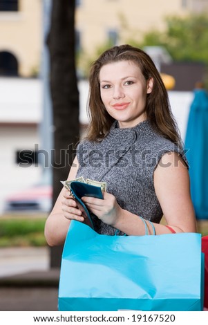 Young woman on a shopping trip holding colorful shopping bags, counting her money, thinking about what else she can buy.