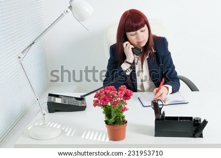 Confident business woman speaks by phone and writes in notebook