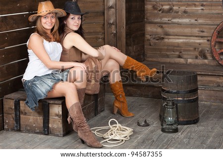 brunette and blonde CowGirls with a ancient cart wheel sitting in old depot