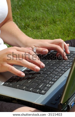 A young woman types on her computer in the grass.