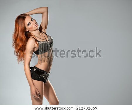 The beautiful neat figure woman with red shiny hair in a suit in rock style poses in the studio