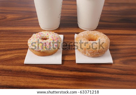 two ring doughnuts on an office desk on napkins and with take away coffees