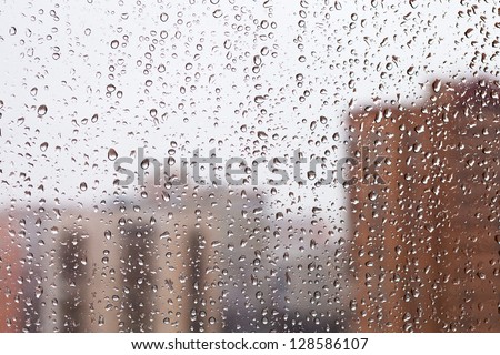 raindrops on home glass window with city buildings background
