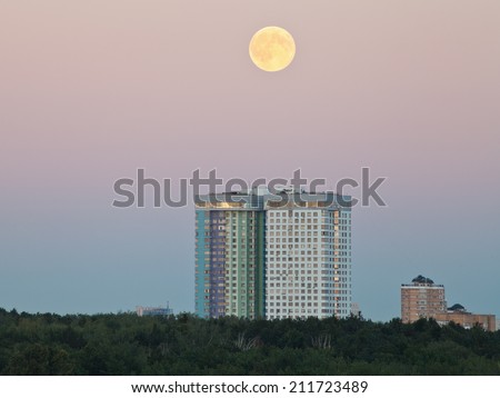 full moon in evening sky over urban houses in summer