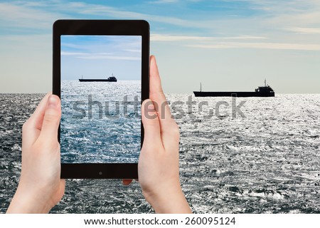 travel concept - tourist taking photo of ship in Black sea in autumn evening on mobile gadget