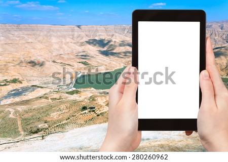 travel concept - tourist photograph valley of Wadi Al Mujib river and dam, Jordan on tablet pc with cut out screen with blank place for advertising logo