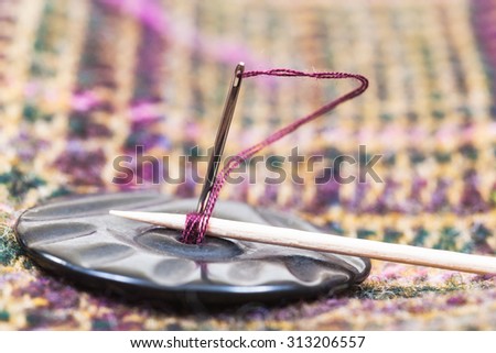 attaching of button to woolen textile with stick by needle close up