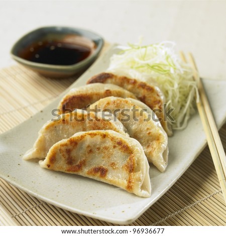 Pan-fried gyoza on white plats with dipping sauce and chopsticks on side.