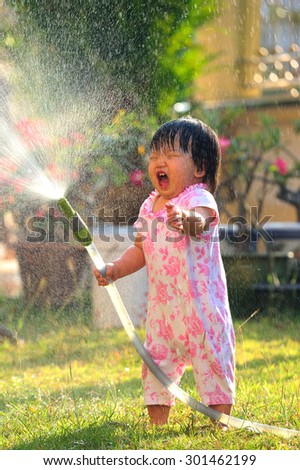 Happy child girl pours water from a house in summer season