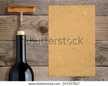 Bottle of wine with corkscrew and blank paper on wooden background