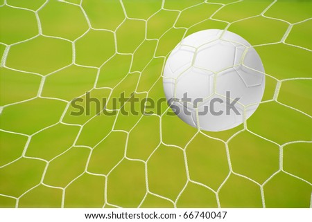 Close-up of a soccer ball (football) going into the back of the net with a green grass background.
