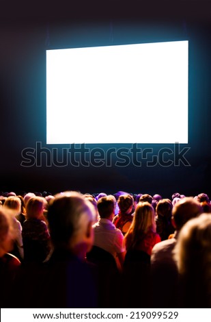 Crowd audience in dark looking at bright screen