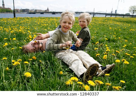 Mother and her sons in meadow with dandelions. Riga city in foreground.